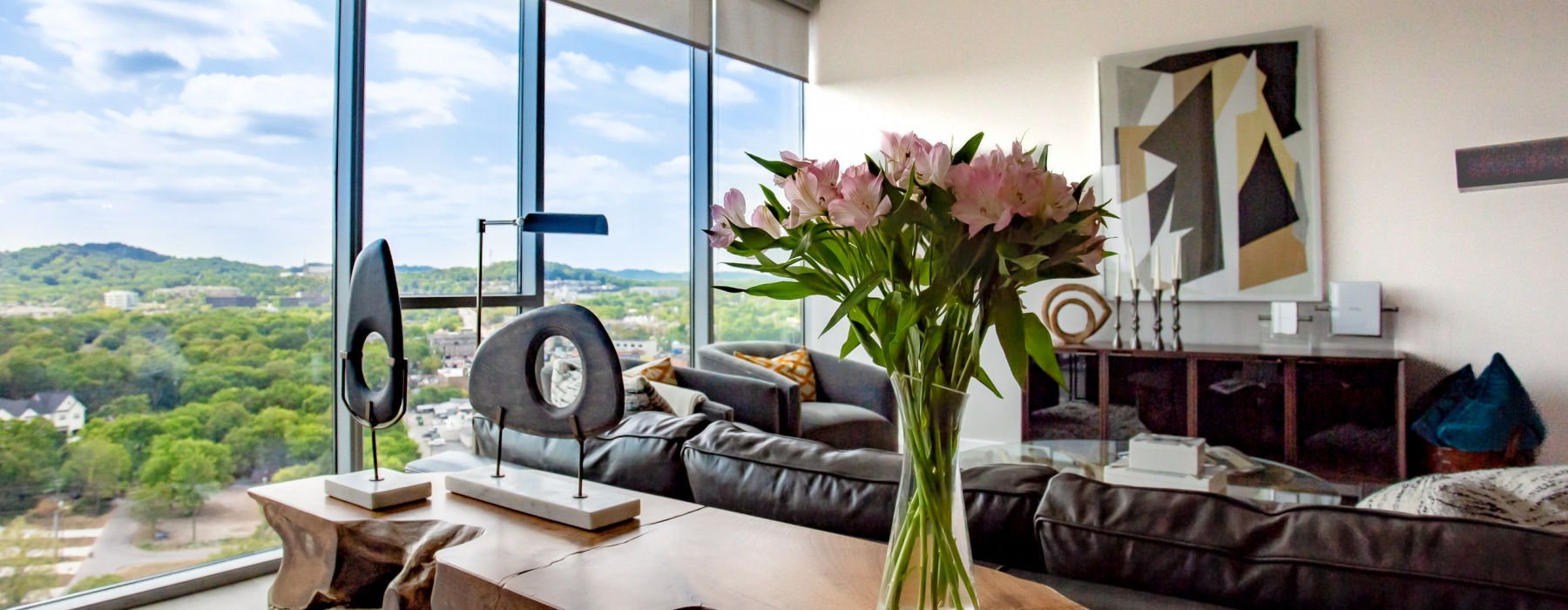 Penthouse living room with view of rolling green hills and vase of flowers