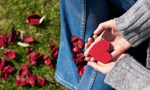 Woman sitting in park holding paper heart